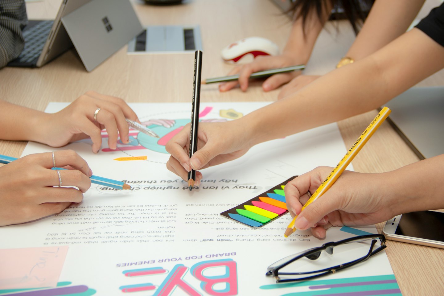 Mani che collaborano a un progetto di design con matite e un laptop.